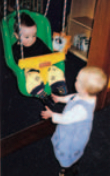 Two infants playing with indoor swing-set