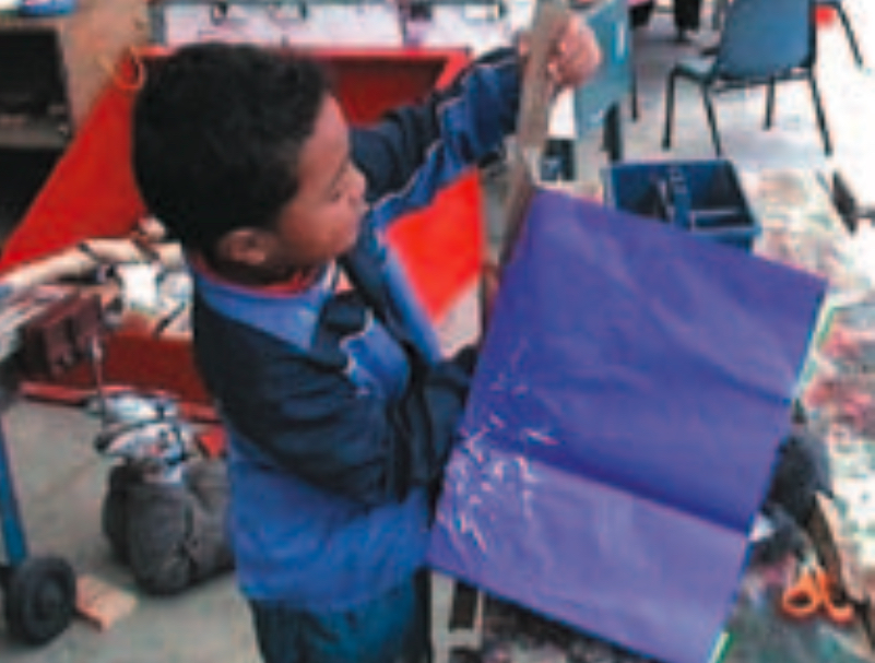 Boy attaching rectangle of purple paper to piece of wood