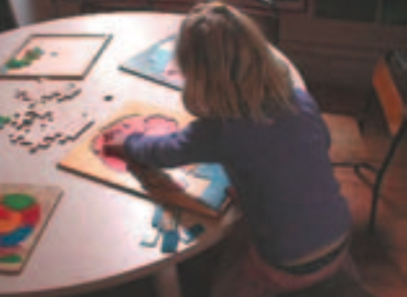 Blond girl doing a puzzle at a table