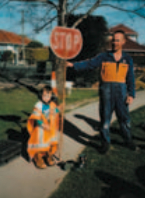 Child wearing safety gear holding a stop sign next to a man in overalls