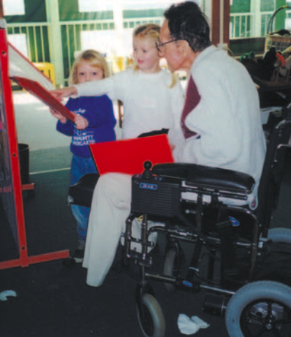 Two blond girls talking a to man in a wheelchair